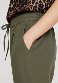 Olivgröna byxor med elastisk midja och dragsko, med sidofickor och en mjuk, slät tygtextur.