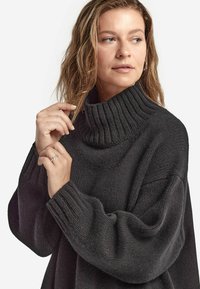 Mörkgrå stickad polotröja med ribbad krage och breda ärmar, med ett texturerat tyg och avslappnad passform.