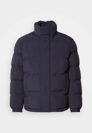Marineblaue Steppjacke mit hohem Kragen, gestepptem Textil und gerippten Bündchen. Mit einem Frontreißverschluss und zwei Seitentaschen.