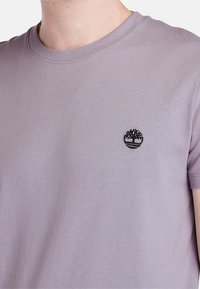 Světle fialové bavlněné tričko s kulatým výstřihem a krátkými rukávy. Na hrudi je umístěno malé černé vyšívané logo.