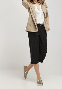 Pantaloni cropped neri con una vestibilità ampia, abbinati a una camicia bianca e a un giubbotto leggero beige. L'outfit presenta sneakers argento con un design testurizzato.