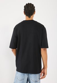 Svart bomull T-skjorte med avslappet passform, korte ermer og rund hals. Modellen har på seg lyseblå denimshorts.