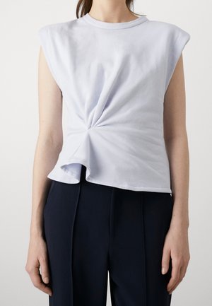 Donna con top senza maniche di un leggero lavanda con dettaglio a nodo attorcigliato in vita e pantaloni blu scuro a vita alta.