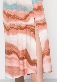 Pitkä mekko, jossa on aaltoilevia kuvioita pinkissä, valkoisessa, ruskeassa ja sinisessä. Kangas näyttää pehmeältä ja siinä on sivureikä lisäyksinä.