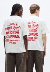 Camisetas blancas de algodón con gráficos rojos llamativos que dicen "Vintage Charm", "Modern Appeal" y "Cali 1985-1985", con mangas cortas.