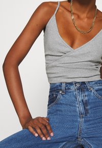 Débardeur gris côtelé avec un décolleté en V profond et des bretelles fines, associé à un jean en denim bleu taille haute avec des coutures apparentes.