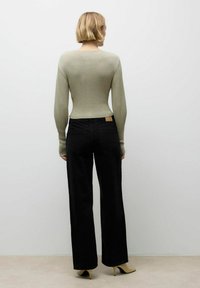 Hele rohelise sooniku musteriga pikkade käistega topp, mis on ühendatud kõrge vöökohaga mustade laia säärega teksadega. Teksadel on vööl silt ja need on mugava lõikega.