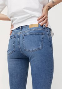 Vaqueros de mezclilla en azul claro con corte ajustado, que cuentan con un parche de cuero en la parte posterior, dos bolsillos traseros y acentos de costura mínimos.