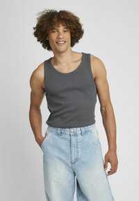 Débardeur gris à côtes avec des bretelles larges, associé à un short en denim bleu clair à coupe ample, doté d'une fermeture à bouton et de poches latérales.