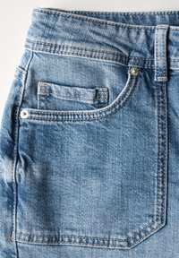 Jeans de mezclilla azul claro con un solo bolsillo trasero, costuras visibles y un botón de metal en la cinturilla. Textura suave y aspecto desgastado.