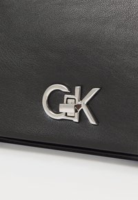 Borsa in pelle nera con texture, caratterizzata da un fermaglio a logo geometrico in tonalità argentata. Il design mette in risalto linee moderne e affusolate con un uso minimale di hardware.