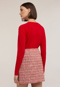 Červený pletený top s dlouhým rukávem spárovaný s mini sukní s vysokým pasem a texturou v teplých odstínech. Mezi detaily se nachází upnutý silueta a jemné vzory.