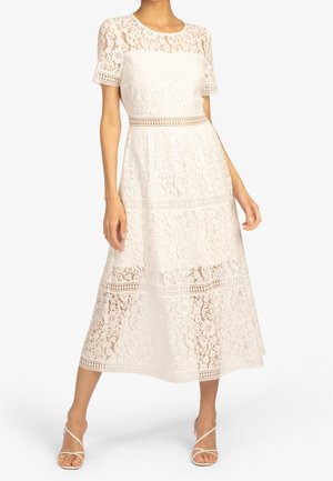 Vit spets midi klänning med korta ärmar, som har blommönster och horisontella skärningar, framhävd av en figursydd midja och en flödande kjol.