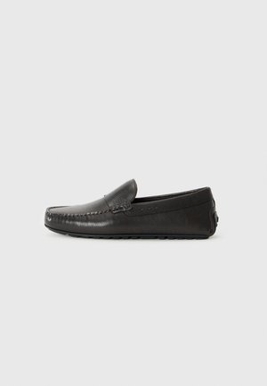 Mocassin noir en cuir avec une finition texturée, présentant un profil bas et des détails de couture subtils. Semelle lisse et design d'accent à l'arrière.