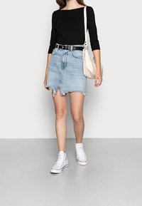 Denim mini skirt with frayed hem, light blue color. Worn with a black fitted top and white high-top sneakers. Accessorized with a beige bag.