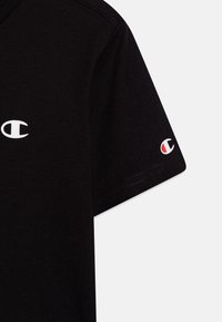 Zwarte katoenen t-shirt met een witte logo aan de voorkant en een kleiner multikleurig logo op de mouw. Korte mouwen en een klassieke snit.