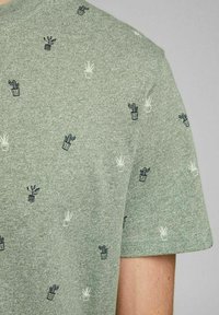 Groene T-shirt met korte mouwen van een gestructureerde brei. Voorzien van een herhalend patroon van kleine geborduurde potplanten in marineblauw en wit.
