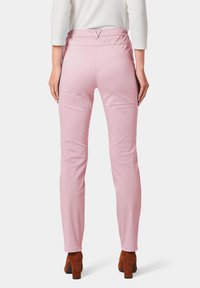 Roze stretchbroek met een gladde textuur, voorzien van een elastische tailleband en een aansluitend ontwerp, gecombineerd met bruine, chunky hakken.