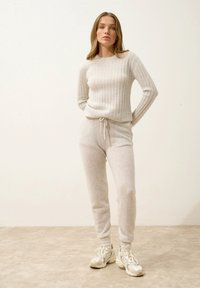 Světlé šedé žebrované pletené svetr kombinovaný s odpovídajícími zúženými tepláky s elastickým pasem na šňůrku. Texturovaná tkanina s jemným vzhledem.