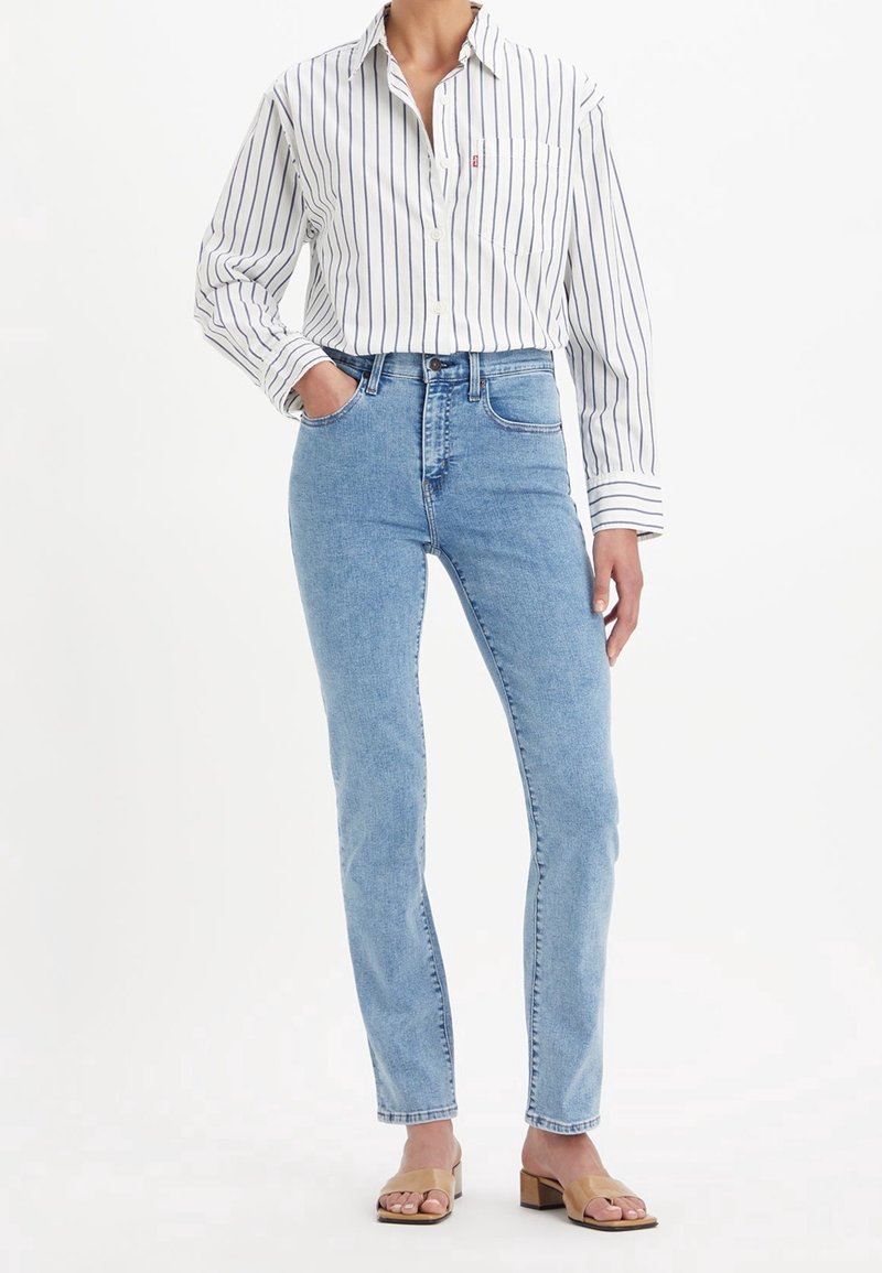 Jeans en denim bleu avec une taille haute et des jambes droites, associés à une chemise blanche à rayures à boutons et des sandales à talons carrés beiges.