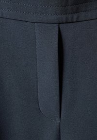 Mörkgrått tyg med en slät textur, som har en liten veck och sydda detaljer vid midjan. Närbild.