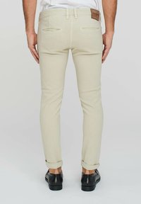 Pantaloni beige slim-fit con tasche posteriori, passanti per cintura e orli arrotolati. Presentano una toppa in pelle sulla vita e una trama in cotone liscia.