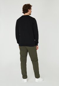 Schwarzes Baumwoll-Sweatshirt mit langen Ärmeln, gerippten Bündchen und Saum, kombiniert mit olivgrünen Hosen und weißen Sneakers. Einfaches, lässiges Design.