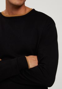 Czarny sweter z okrągłym dekoltem i kontrastowym brązowym ściągaczem. Materiał wydaje się gładki i elastyczny, z dopasowanymi mankietami.