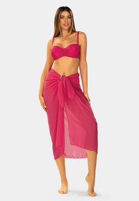 Różowy biustonosz bikini z marszczeniami i regulowanymi ramiączkami, zestawiony z przejrzystym, różowym sarongiem związanym w talii z okrągłym akcentem.