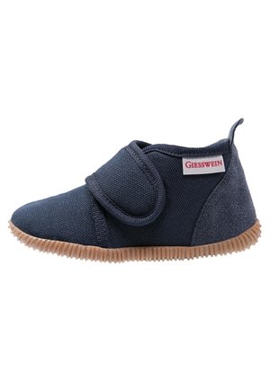 Chaussure bébé bleu marine en tissu texturé, sangle à fermeture auto-agrippante, semelle rainurée marron clair et étiquette de la marque Giesswein sur le côté.