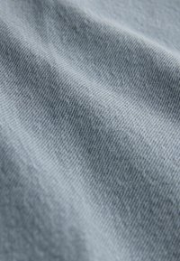 Helle blaue Denim-Stoff mit glatter Textur, der ein dezentes gewebtes Muster und leichte Farbintensitätsvariationen aufweist.