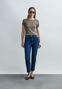 Pruun soonikuga t-särk, sinised teksapüksid ja pruunid madalad kingad. Outfit on lõdva lõikega, varrukad on üles keeratud ja disain on klassikalise sirge lõikega.