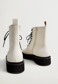 Botas de tobillo de imitación de piel de oveja blancas con una suela de plataforma negra, que cuentan con cordones en la parte frontal y cremalleras en los laterales. Punta redondeada y tira en la parte trasera.