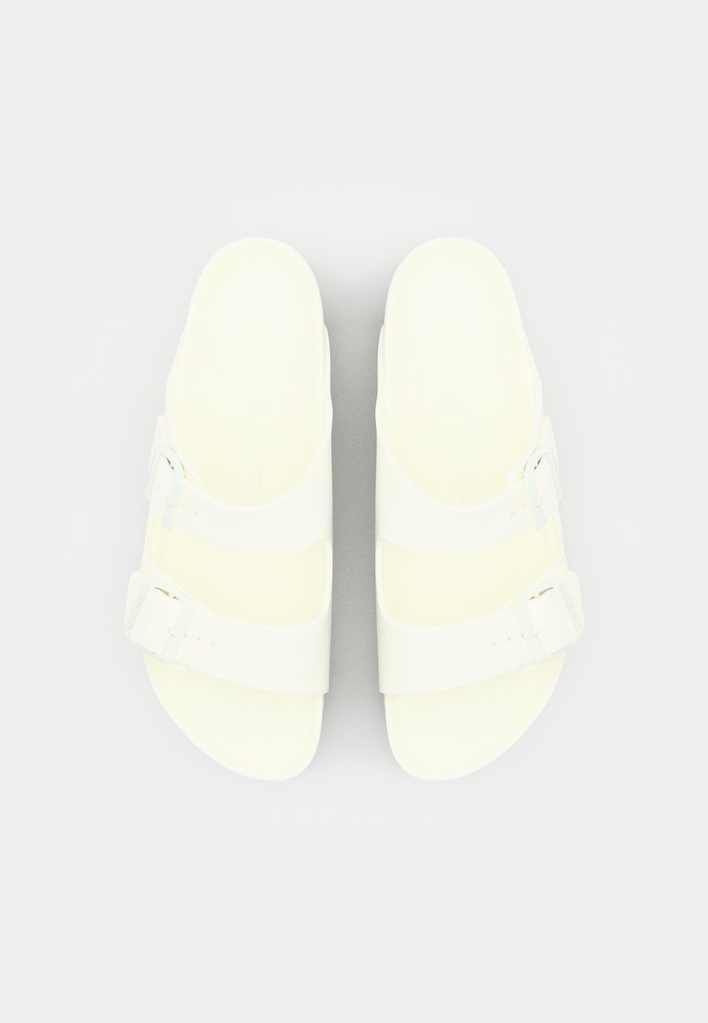 Sandalias blancas con dos correas ajustables y herrajes de hebilla. Textura suave y forma contorneada para mayor comodidad. Diseño de suela plana.