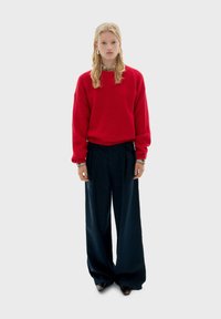 Rode gebreide trui, ruime pasvorm, gecombineerd met marineblauwe high-waisted wijde broek. Accessoires zijn dunne armbanden en oorbellen.