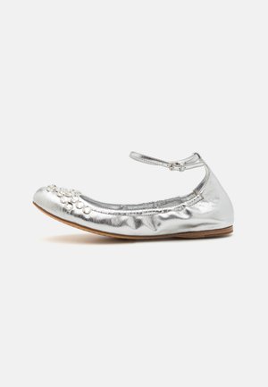 Ballerines métalliques argentées avec une bride de cheville et des embellissements floraux décoratifs sur le bout. Surface en cuir lisse et forme arrondie.