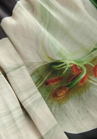 Seidenstoff mit einem floralen Druck in Grün, Beige und Rot. Das Design umfasst zarte Blütenblätter und auffällige Staubgefäße.