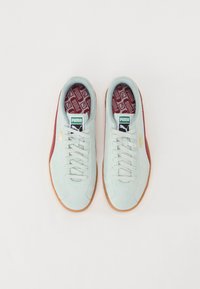 Lyseblå semsket sneakers med hvite lisser, med et rødt aksentstripe og mønstret maroon innersåle. Gummigummisåle. PUMA-logo vist.