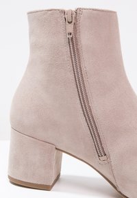 Bottine beige en suède avec un talon bloc et une fermeture éclair sur le côté, sur un fond blanc uni.