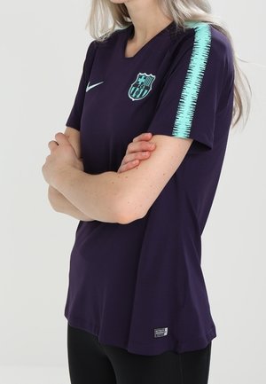 Person trägt ein dunkelviolettes Barcelona-Fußballtrikot mit türkisfarbenen Schulterstreifen, Nike-Logo und Vereinswappen auf der Brust.