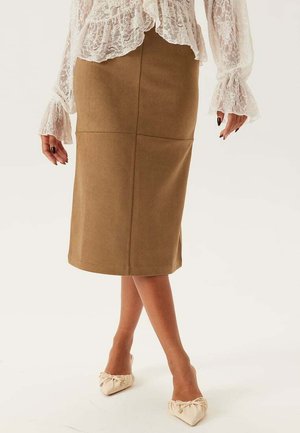 Bruine pencilrok van zacht materiaal, met naaddetails en een lengte tot op de knie. Gecombineerd met beige flats met strikaccent.