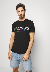 Sort T-shirt med farverig "CARLO COLUCCI MILANO ITALY" grafik, rund halsudskæring, korte ærmer og en blød bomuldsstruktur.