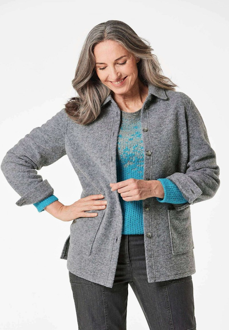 Graue Wollmischung Button-up Jacke mit Kragen, ausgestattet mit Taschen, aufgerollten Bündchen und über einem türkisfarbenen, gemusterten Pullover getragen.