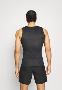 Débardeur de sport noir sans manches avec un tissu texturé. Design ajusté, mettant en valeur la musculature du dos, associé à un short noir.