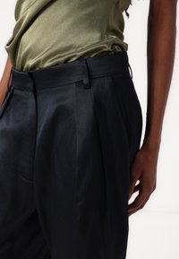 Pantalons plissés bleu foncé en tissu léger avec une texture lisse. Présente une coupe droite et des poches latérales.