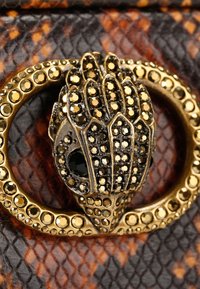 Metalen sluiting met een gedetailleerd handontwerp versierd met gouden en zwarte rhinestones, geplaatst tegen een gestructureerde patroonachtergrond.