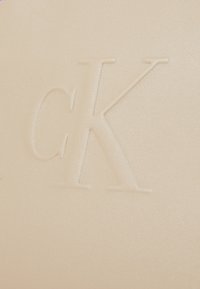 Portafoglio in pelle beige con logo "CK" in rilievo. Tessuto liscio con una leggera lucentezza e bordi arrotondati.