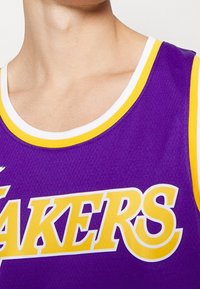 Canotta da basket viola con rifiniture gialle e "LAKERS" in caratteri in grassetto. Il tessuto è in rete, mostrando una finitura testurizzata.