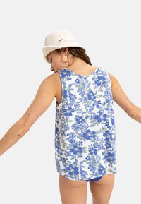 Blomstret tanktop i hvid, med blå og grønne mønstre. Ærmeløs design med en løs pasform og en buet kant.