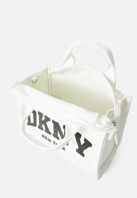 Borsa a spalla in tela bianca con logo "DKNY" nero, chiusura con zip, due manici e superficie testurizzata. Design interno aperto per lo stoccaggio.